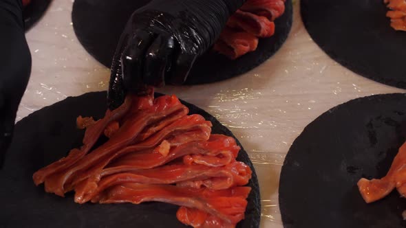 Palm Hands in Black Gloves Put Delicious Sliced Salmon Fish on Stone Plates Range Pieces of Fish alt