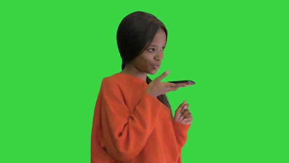 Pretty African American Woman in Bright Jumper Dictating Message Using Her Phone on a Green Screen alt