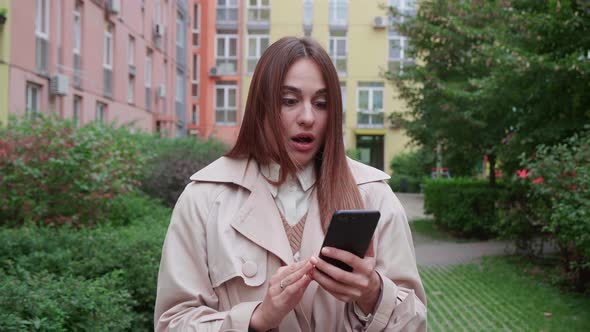 Happy Fun Charismatic Young Brunette Woman Holding Smartphone Near Building Background alt