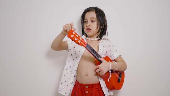 Musician Hawaiian Child Boy with Long Hair Shirt with a Red Small Guitar Playing Against White Wall alt