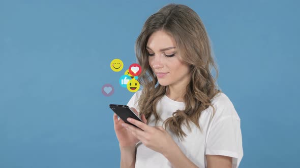 Young Woman Using Smartphone Isolated on Blue Background, Flying Smileys, Emojis and Likes alt