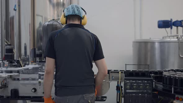 Back View Of An Operator Wearing Hairnet And Headphones Working In A Beer Factory alt