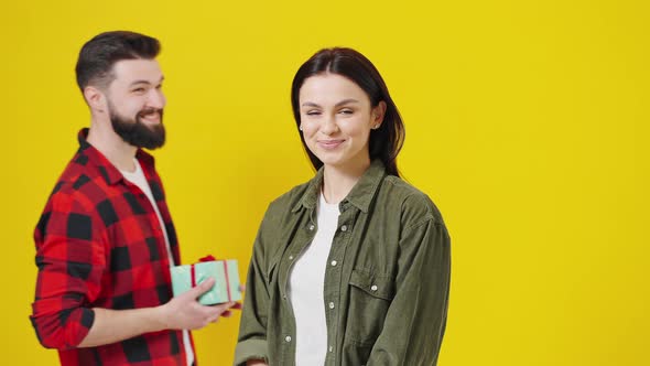 Handsome Male Giving Present to Lovely Young Female Looking Surprised on Yellow Background alt
