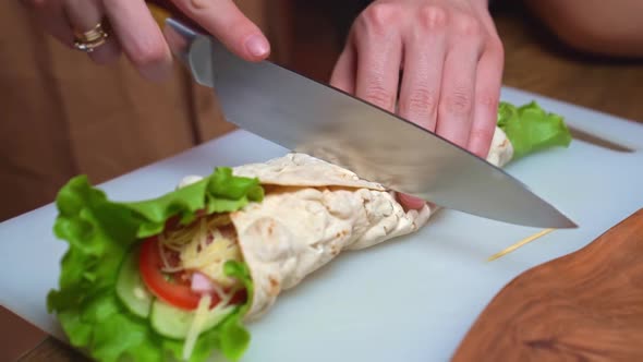 Women's Hands Cut in Half Pita with Vegetables and Cheese on a Cutting Board alt