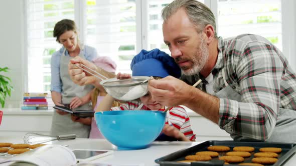 Father helping boy to filter flour using a strainer alt