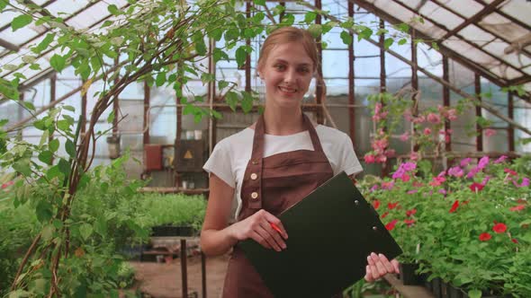 Female Gardener Checks Quality of Plants Takes Notes on Digital Tablet Walking Along Garden Center