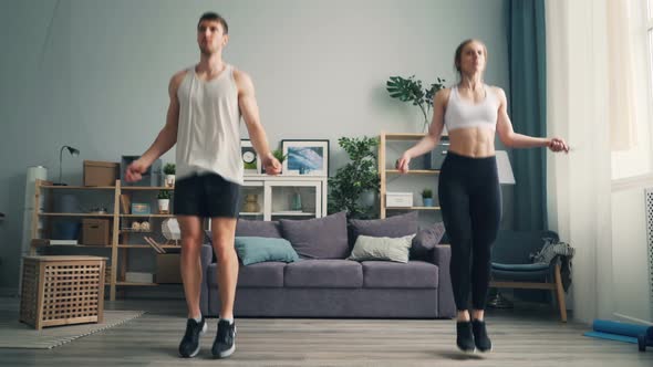 Attractive Girl and Guy Jumping Rope in Studio Apartment Focused on Exercise alt