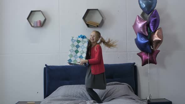 Birthday Teen Girl Jumping on Bed Holding Gift Box alt