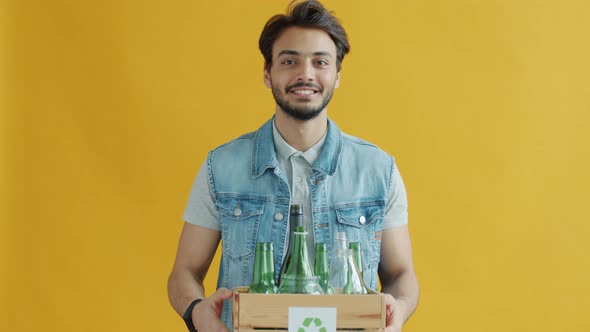 Slow Motion Portrait of Middle Eastern Man Holding Box of Glass Bottles with Recycling Sign alt