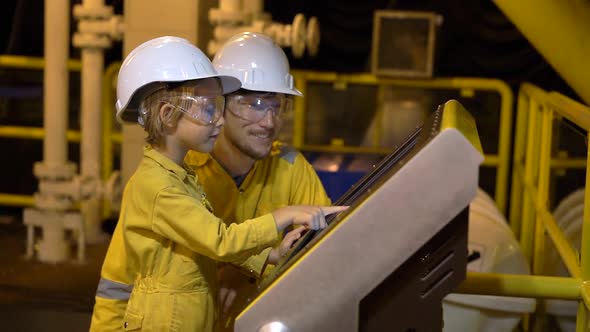 A Young Man and a Little Boy Are Both in a Yellow Work Uniform, Glasses, and Helmet in an Industrial alt