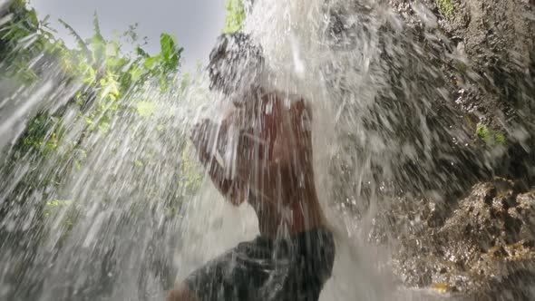 A Young Athlete Does Squat Exercises Under a Strong Waterfall Jet Against the Background of a
