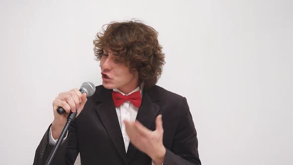 A Man in a Suit with a Red Bow Tie Holds a Microphone Against an Isolated Background