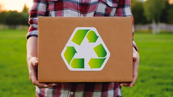 Unidentified woman holds a cardboard box labeled recyclable raw material