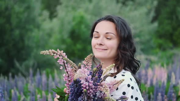 Young Beautiful Woman Posing in a Field with a Bouquet of Lilac Flowers. Happy Brunette in a Field alt