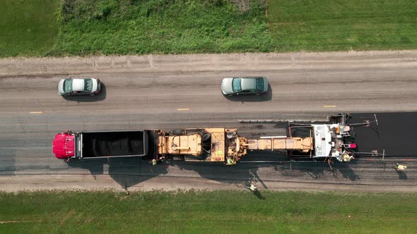 top down view of repaving crew working slowly on the previously prepared roadway to lay asphalt.