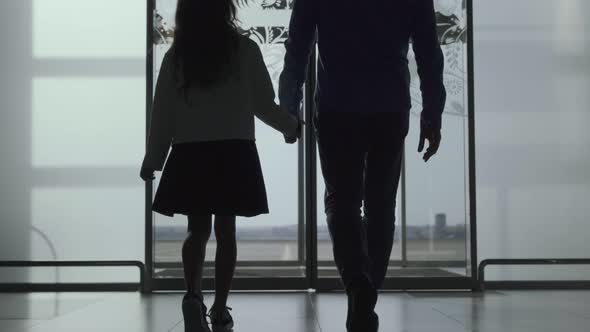 Silhouettes of Caucasian Man and Girl Walking Out the Airport Through Glass Door alt