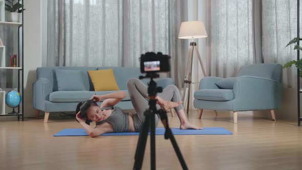Asian Trainer Female In Sports Clothes Speaking To Camera And Doing Crisscross Crunch Workout alt