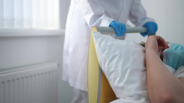 Unrecognizable Nurse Pushing Bed with Patient in Ward Leaving alt
