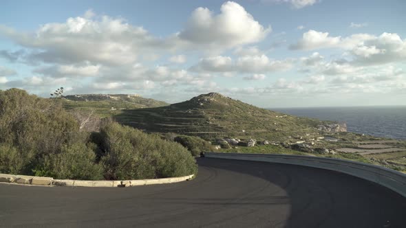 Curvy Asphalt Road Leading Down Near Coastline of Malta with Vast Greenery on Plateu alt