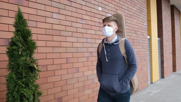 Young Man Put on the Medicinal Mask and Walking Outside with the Guitar in the Back alt