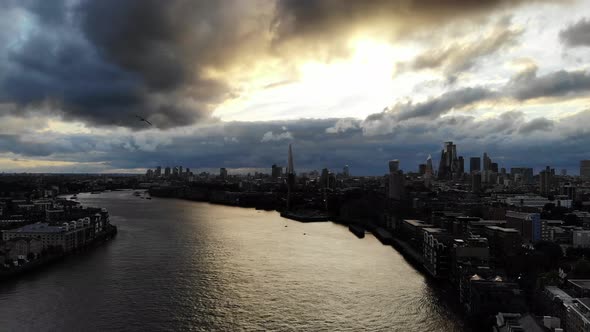 Reverse aerial view of London skyline under dramatic stormy dark clouds flying over river Thames alt