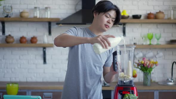 Middle Shot Portrait of Young Man Pouring Milk in Blender with Chopped Banana alt