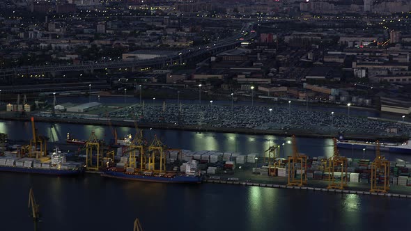 Flying Over Sea Cargo Port with Tanker Transport Ships and Big Yellow Cargo Cranes at Night Against