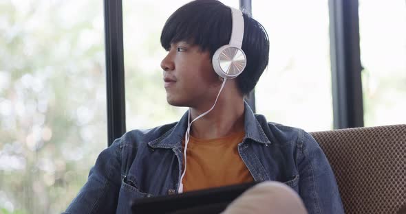 Happy young Asian man listening for music with headphone in living room. alt