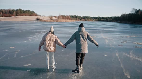 Aerial Shot of Couple Skating on a Clear Frozen Lake on a Sunny Winter Day