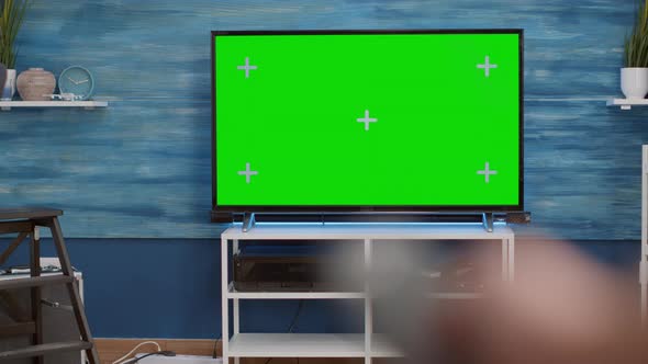 Selective Focus of Hand Holding Remote Control and Switching Channels on Green Screen Tv alt