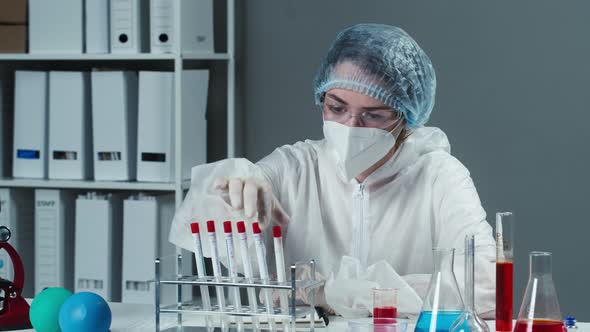 Doctor Wearing Protective Mask Gown and Gloves Taking PCR Tests and Writing Results in Notes alt