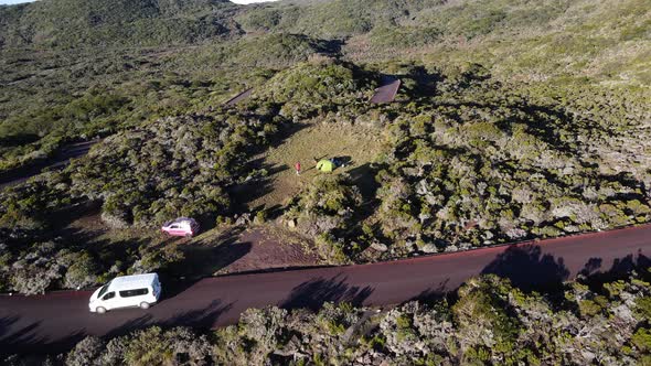 Drone footage of a tent in the mountain with a road and some cars. alt