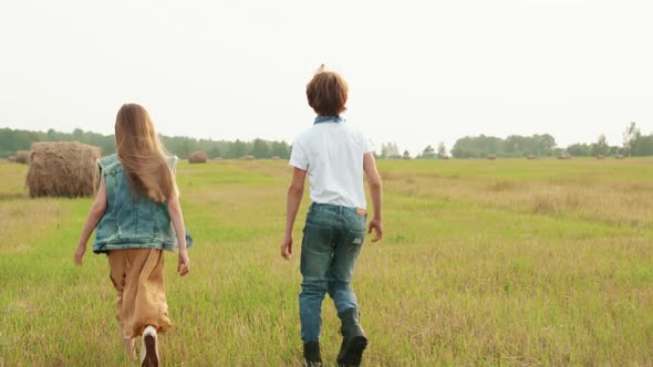 Teenager Boy and Girl Walking on Harvesting Field on Haystack Background alt