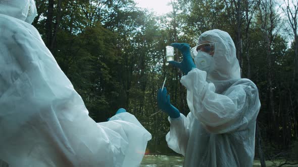 Chemists in Ppe Looking at Water Analysis From Swamp Using Flask and Pipette Wearing Protective Suit alt