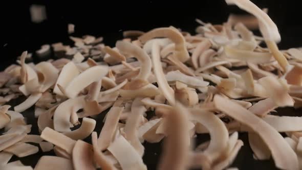 Coconut chips are falling down to the table, close-up, black background alt