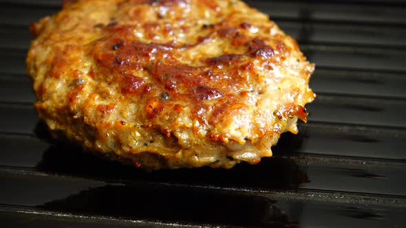 The fried cutlet for hamburger rotates on the grill pan. alt