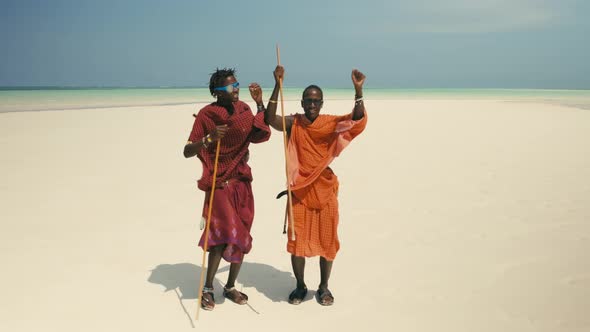 Young Happy Masai Tribe Members in Red Dresses and Sunglasses Dancing on the Sand Beach
