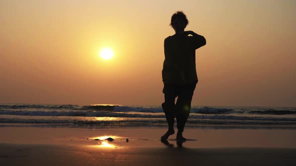 Silhouette of Active Senior Woman Practicing Tai Chi Gymnastic on Sandy Beach. alt