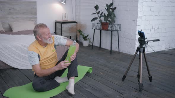 Vlogger, Sports Old Man Blogger Records Video Review of Sports Drink for Blog on Smartphone alt