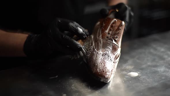 Closeup Hands of Shoemaker in Black Gloves Applying Cleaning Foam on Old Light Brown Leather Shoes alt