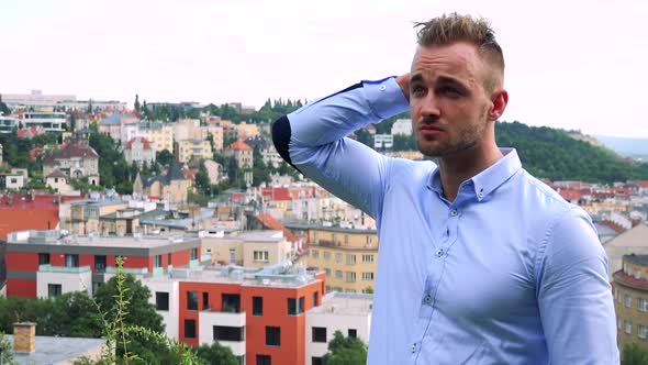 Young Handsome Business Man Thinks About Something (Run Hand Through Hair) - City in Background alt