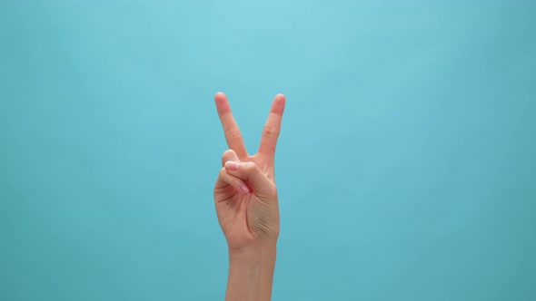 Woman raising two fingers up on hand on the blue background. Concept victory symbol. alt