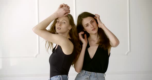 Two Slender Girls, One Blonde, the Other Brunette Posing for the Camera in the White Studio. They alt