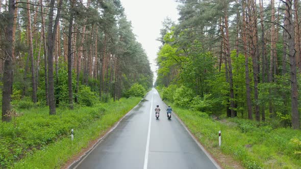 Drone Raising Over Wet Road with Two Motorcyclists Riding Away on Scooters. Extreme Wide Shot of Two alt