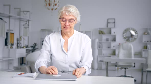 Exhausted senior businesswoman with grey hair closes laptop alt
