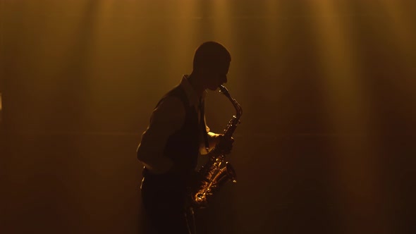 Silhouette a Young Stylish Guy Plays the Golden Shiny Saxophone in the Yellow Spotlights on Stage alt