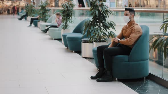 Young Indian Guy in Medical Mask Protecting Health During Pandemic Sitting in Armchair Indoors in alt