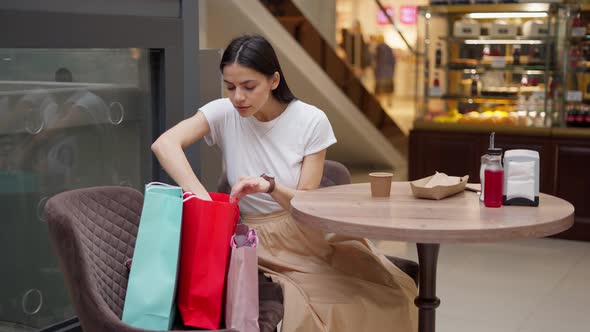 Sitisfied Female in Stylish Outfit Checking Her Purchases in Paper Bags During Lunch at Food Court alt