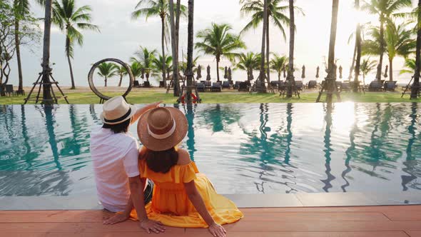 Young couple traveler relaxing and enjoying the sunset by a tropical resort pool alt