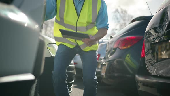 Mature male loss adjuster wearing hi-vis safety vest standing in compound for damaged cars